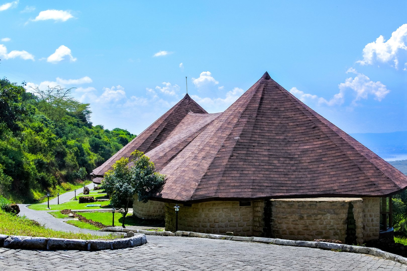 A beautiful lodge with a unique roof design surrounded by lush greenery and a clear blue sky.