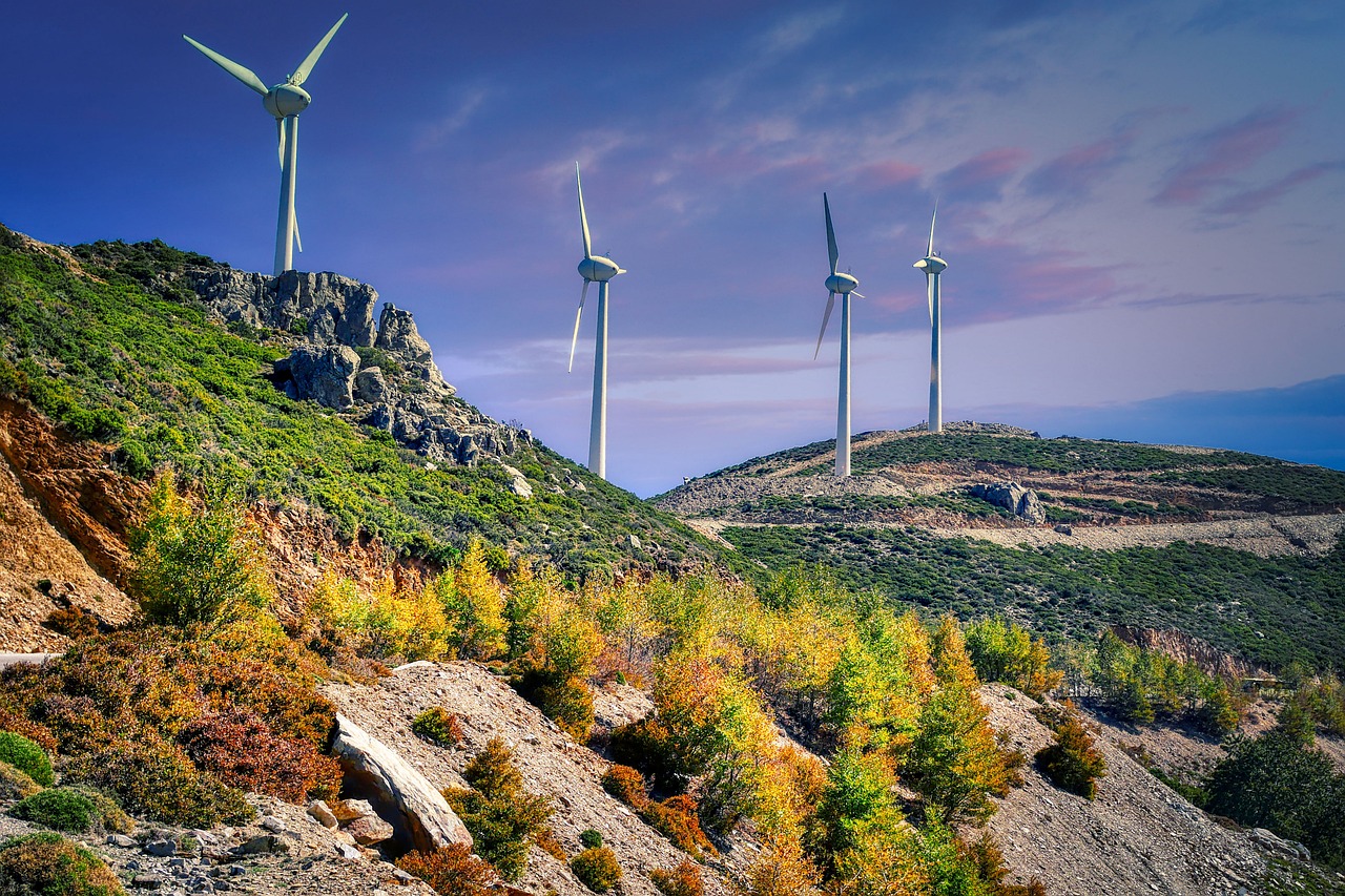 Wind turbines on a hillside with rocky terrain and green vegetation under a blue sky with pink clouds.
