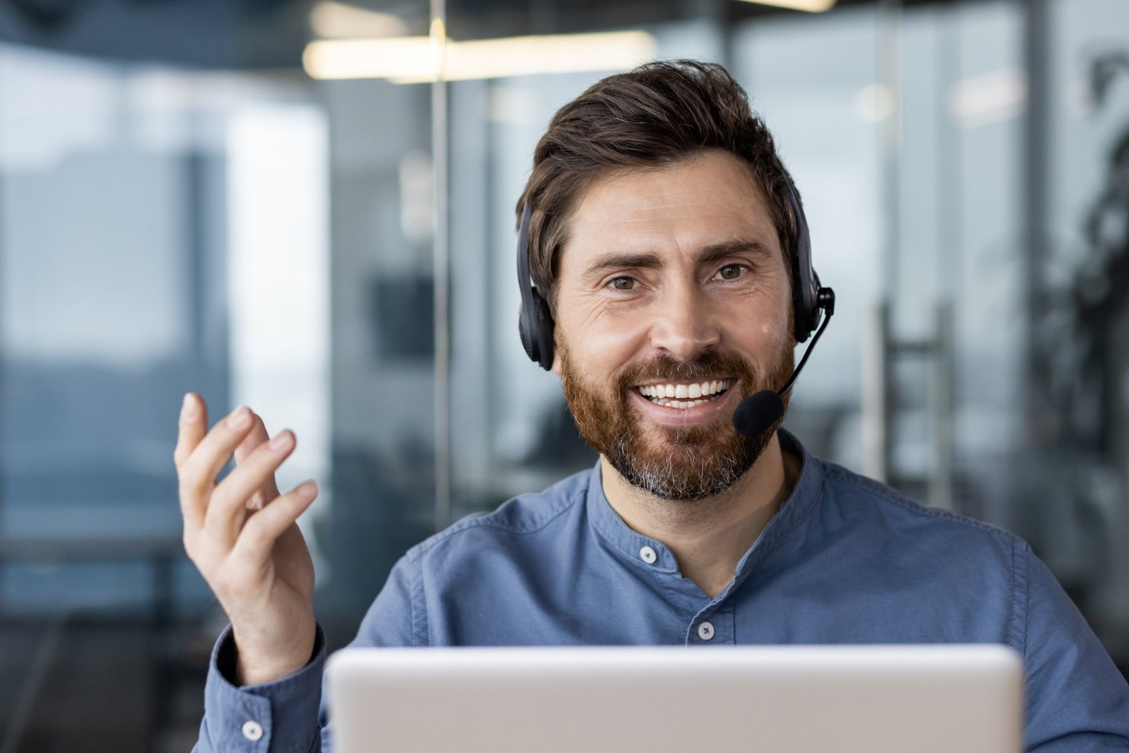 Happy businessman wearing headset smiling during video call in office. Confident man with laptop engaging in virtual meeting. Remote work, customer support and communication concept.
