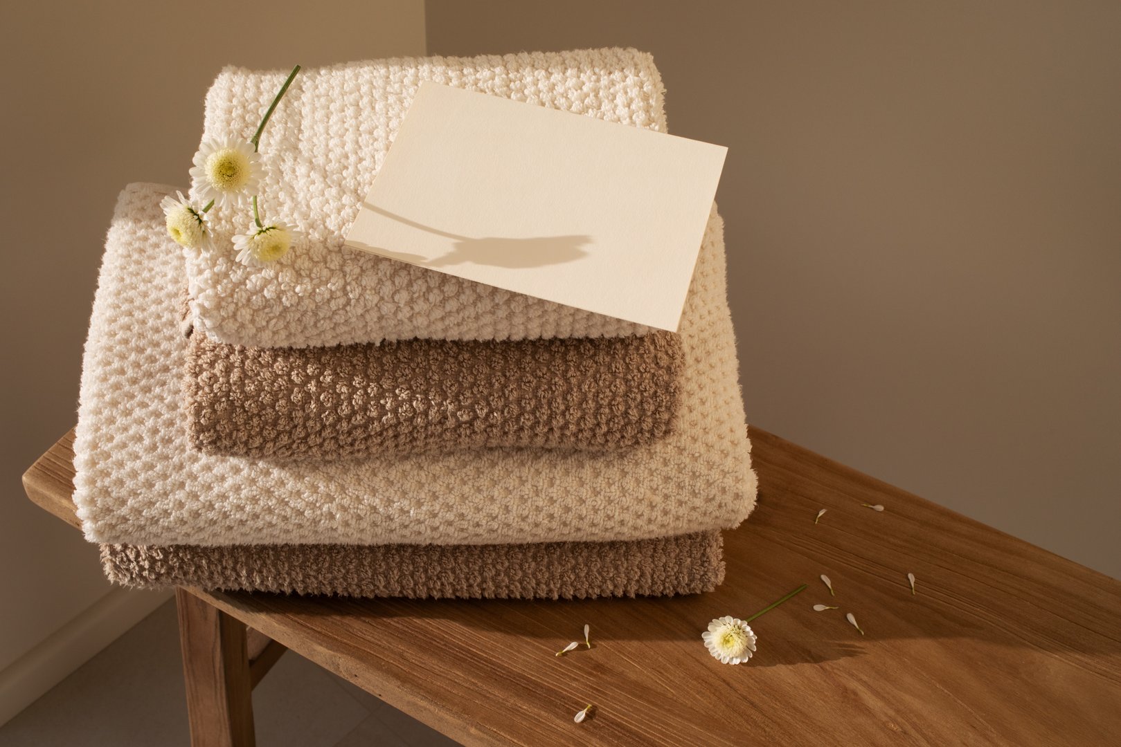 Stack of towels in neutral colors and paper blank in modern aesthetic interior. Fabric bathroom accessories for hygiene, spa and skin care beauty treatment.