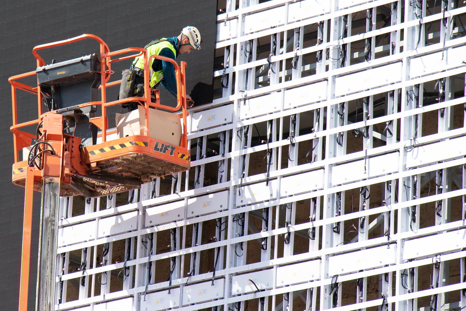 Belgrade, Serbia - May 6, 2020: Construction worker in crane basket installing sheets cladding for covering metal structure on a building facade wall