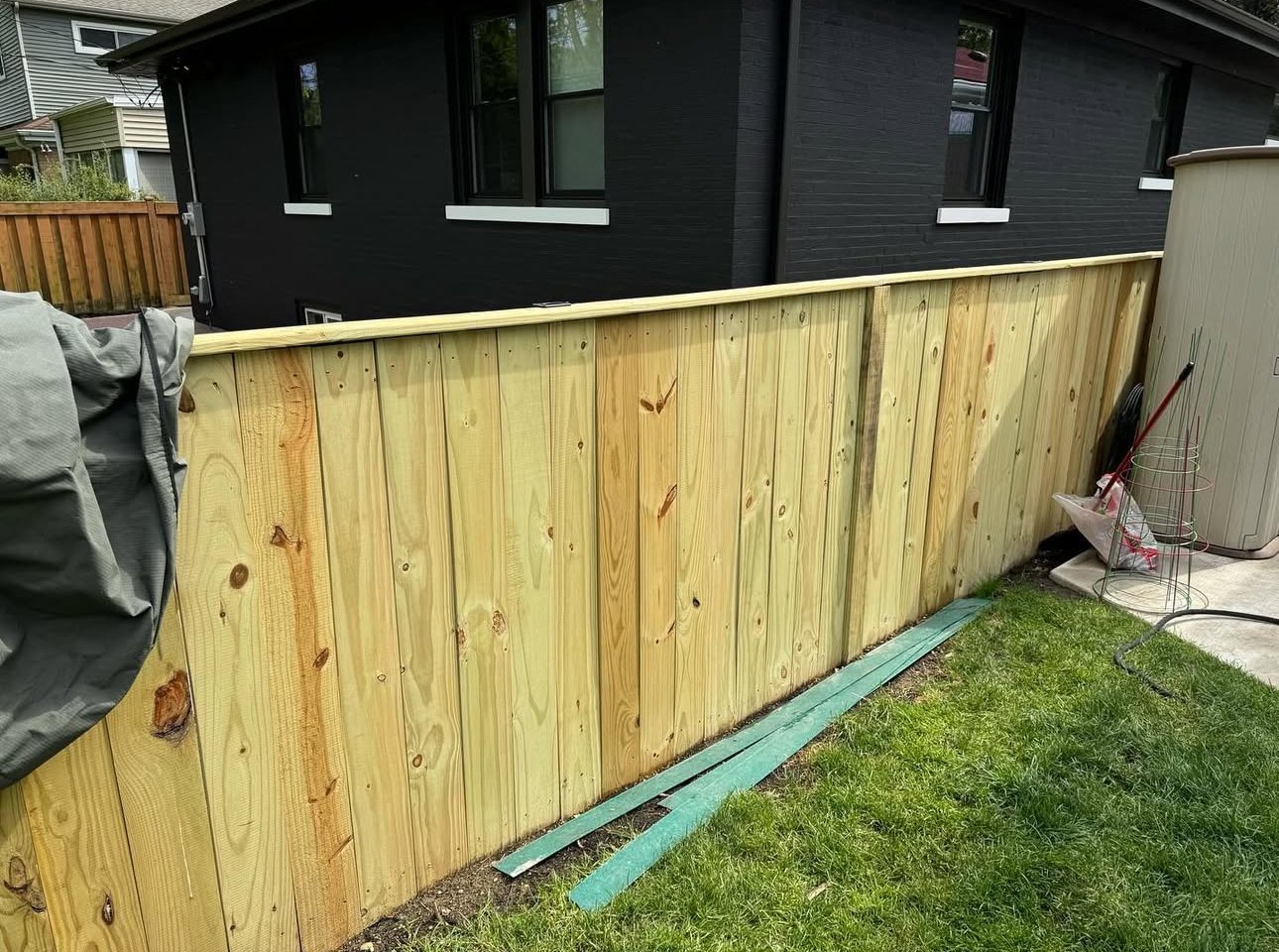 A newly installed wooden fence in a backyard with green grass and a black building in the background.