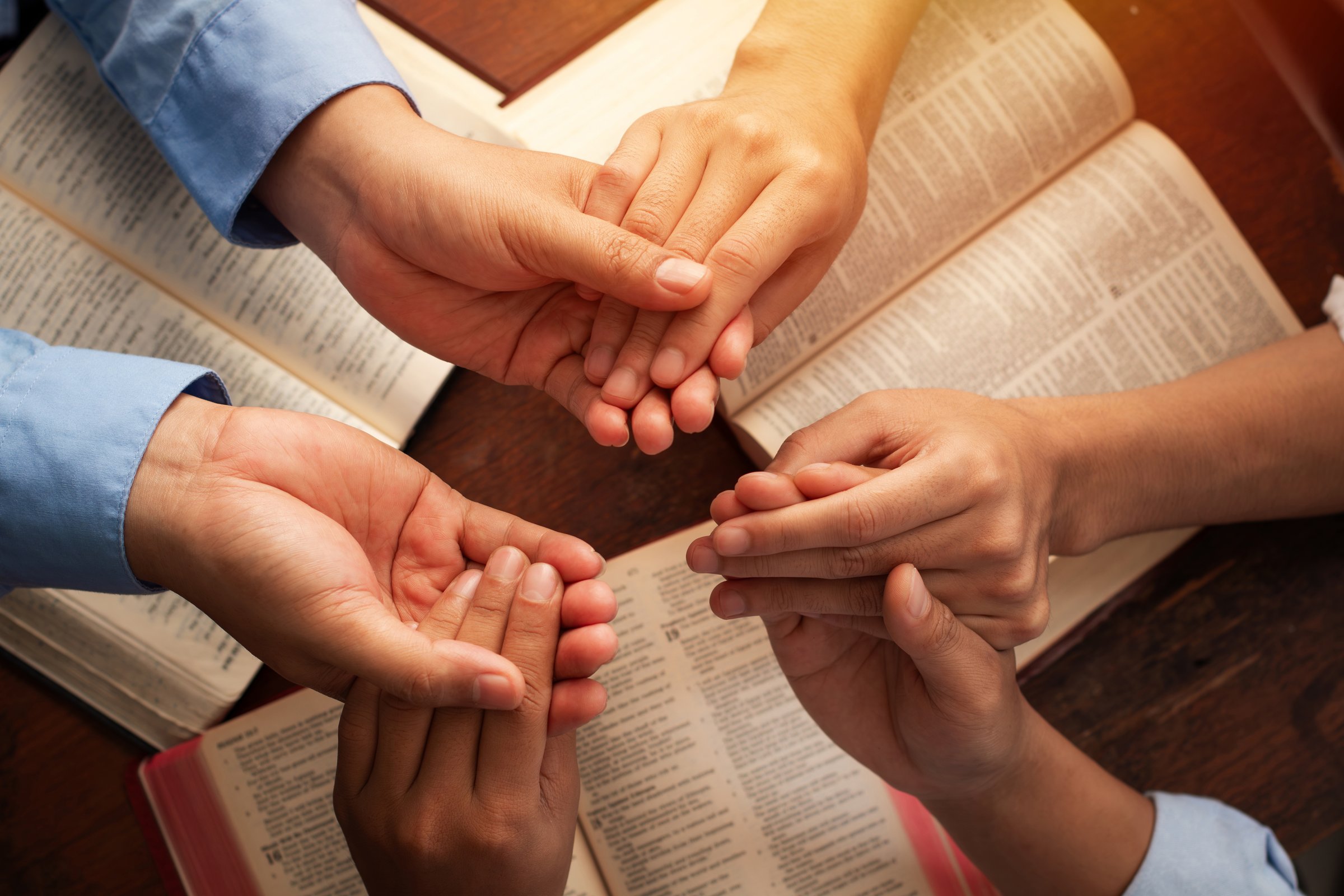 Group of Christian holding hands praying worship together around a wooden table with open Holy Bible page for devotional or prayer meeting concept. Sharing the gospel. Bible study.