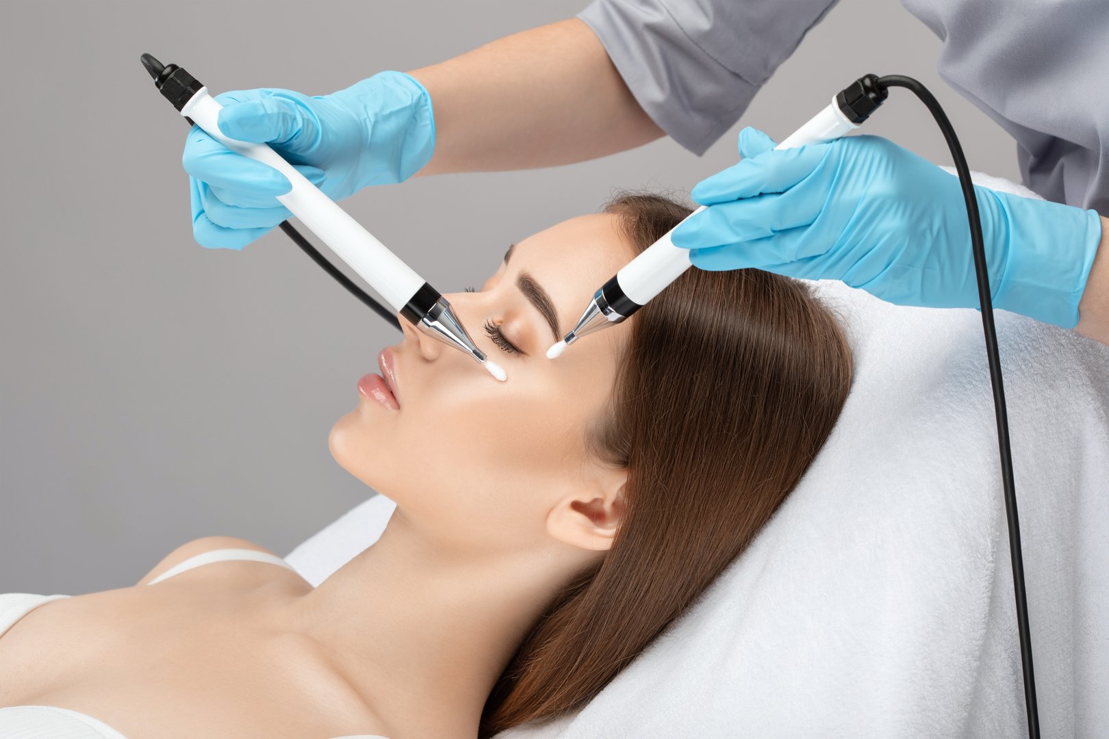 A doctor cosmetologist makes a microcurrent facial therapy to a young woman with a device in a beauty wellness salon.Cosmetology and professional skin care.