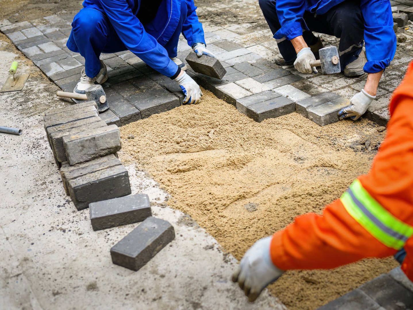 Workers laying brick pavers on the sidewalk.  Road paving and maintenance.