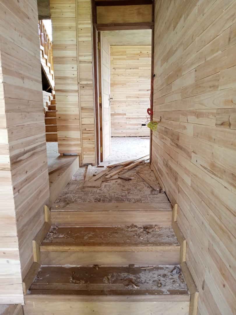 Unfinished wooden interior with stairs, open door, and scattered wood debris on the floor.