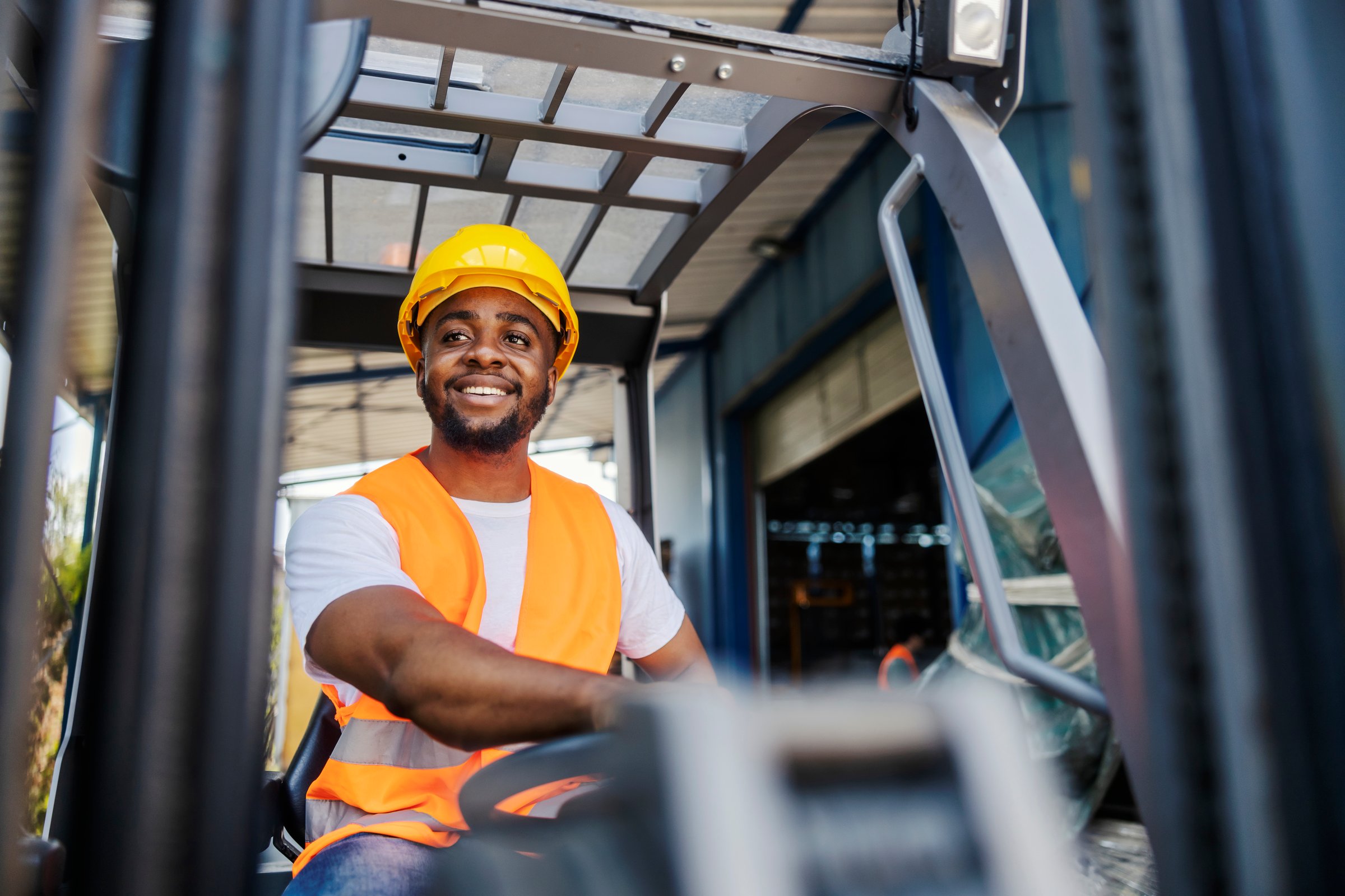 Portrait of smiling diverse forklift operator driving forklift at industry zone.
