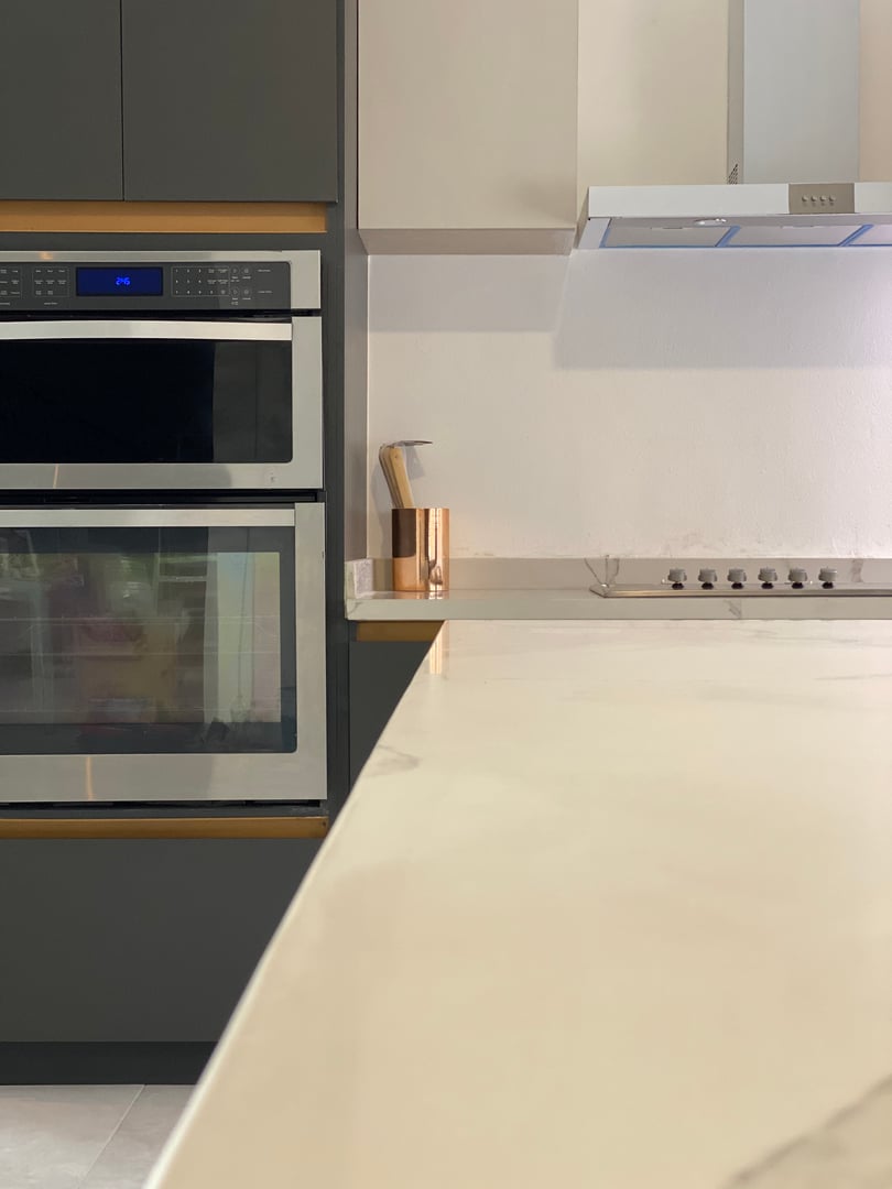 Modern kitchen with double wall oven, marble countertop, and stove. A copper utensil holder is on the counter.