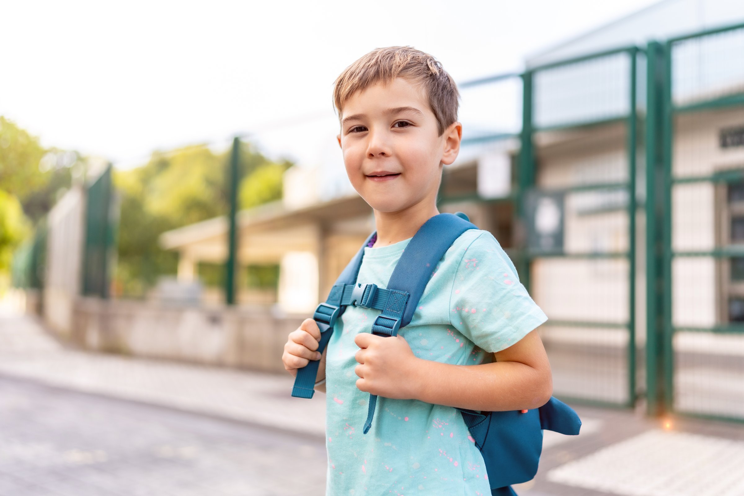 Portrait of a proud boy smiling at camera standing next to school entrance building at first day of school