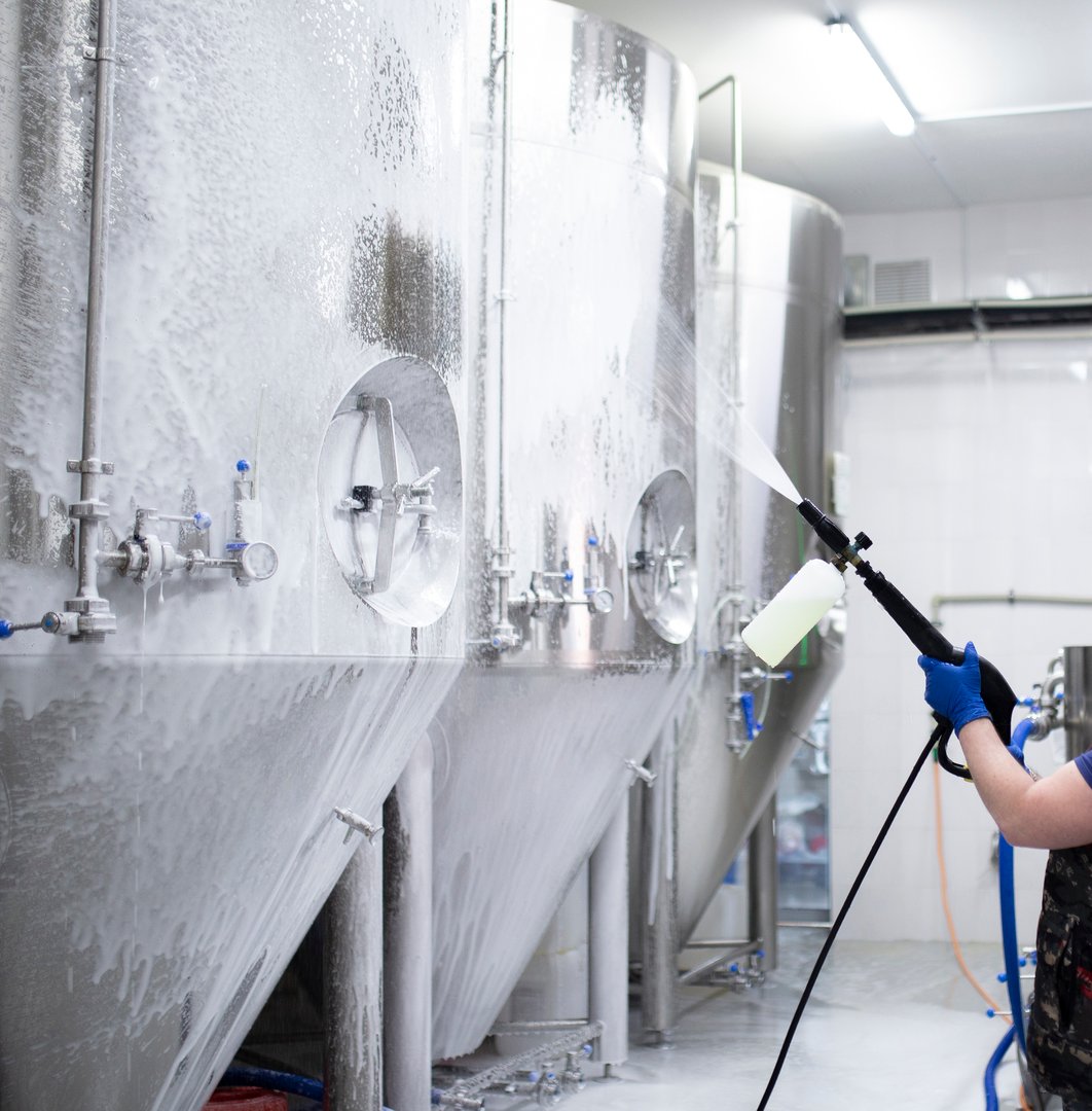 worker's hand hold a high pressure cleaner gun and put foam on equipment on the factory
