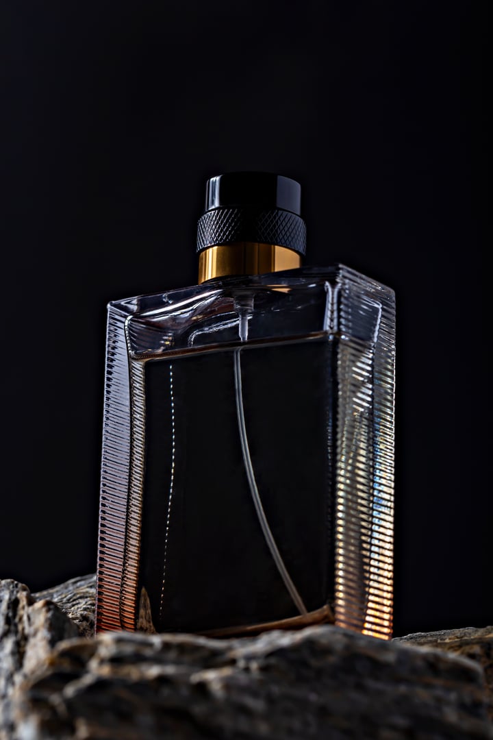 Luxurious black perfume bottle with textured design, highlighted by golden accents, placed on rocky surface against dark background. Perfect for advertising and product presentations