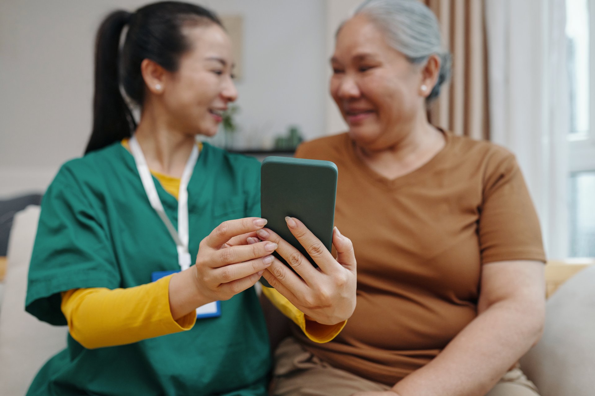 Nurse showing apps in mobile phone to senior woman while they sitting in the room