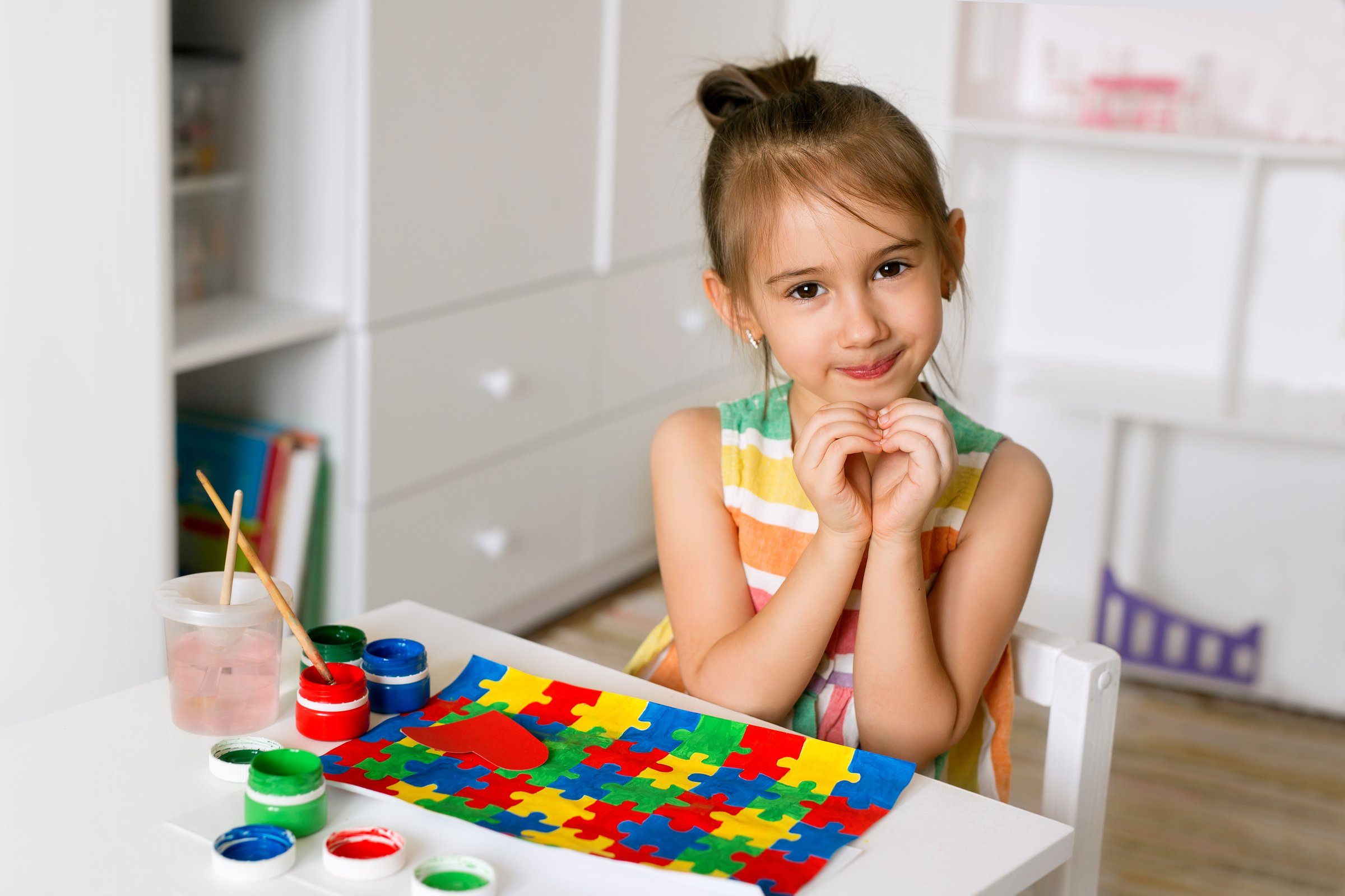 Pretty cute little girl sweetly folded her hands in the shape of a heart as a sign of support for people with autism. Concept of World Autism Awareness Day. Child drew a picture with puzzles