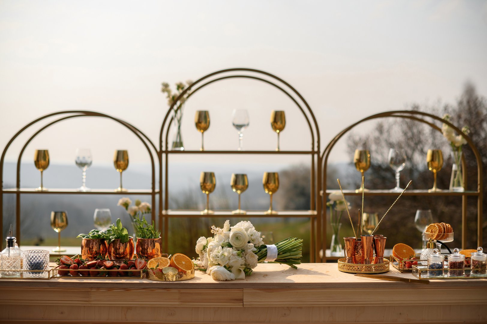 Elegant outdoor bar setup with gold accents and floral wedding bouquet.