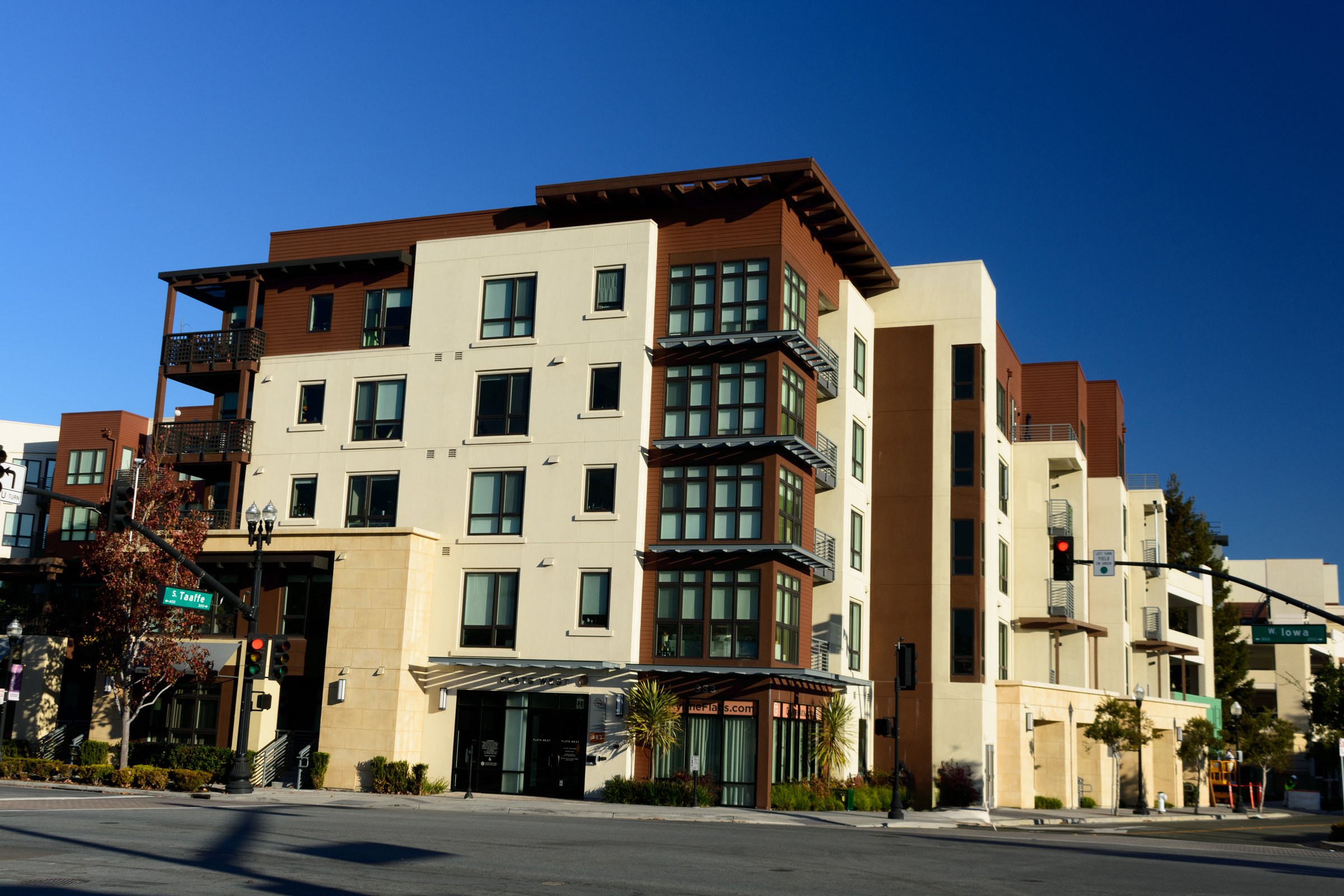 Modern mid-rise apartment building with beige and brown tones, large windows, and balconies