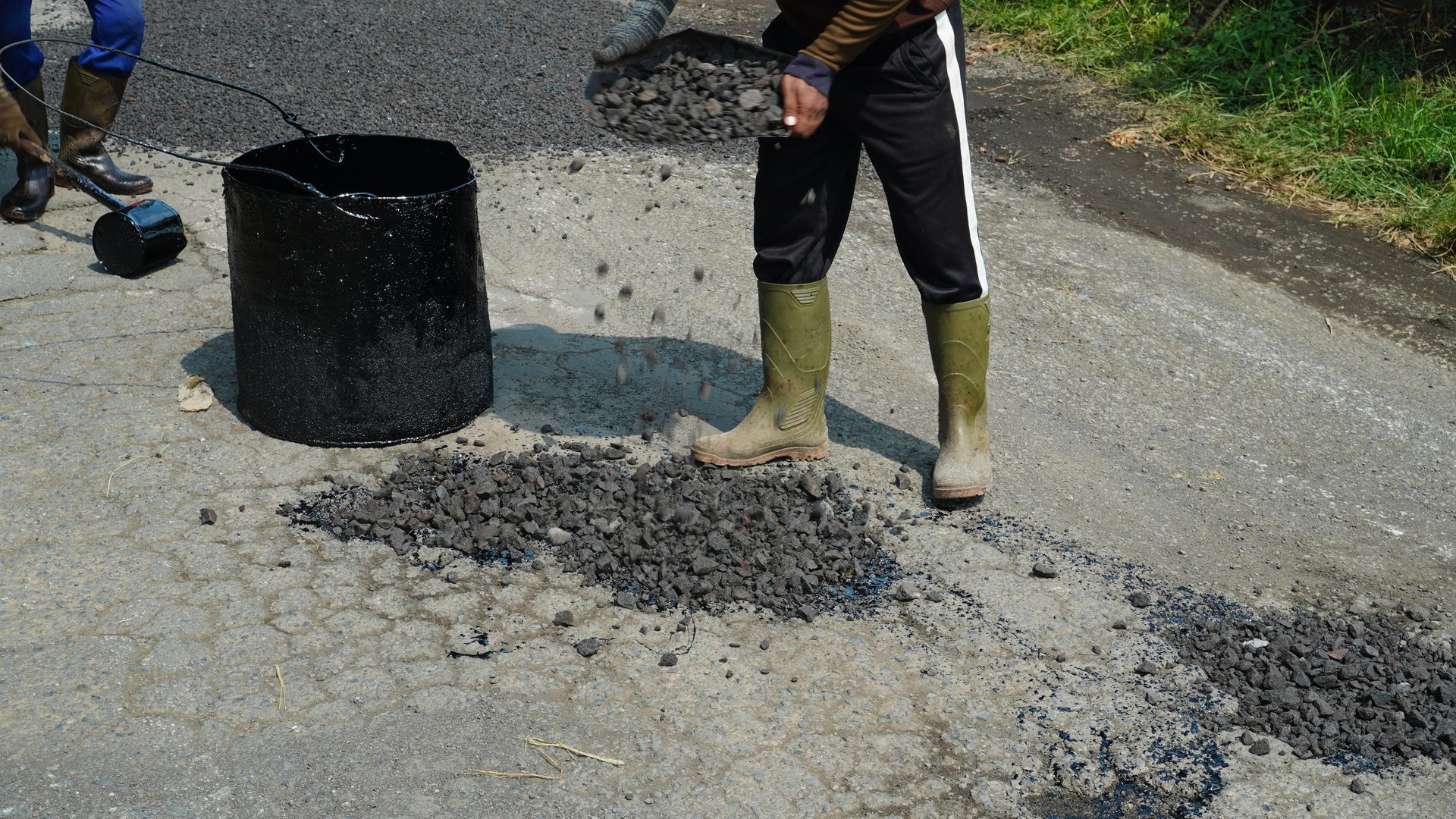 workers pour gravel in the process of repairing a potholed asphalt road