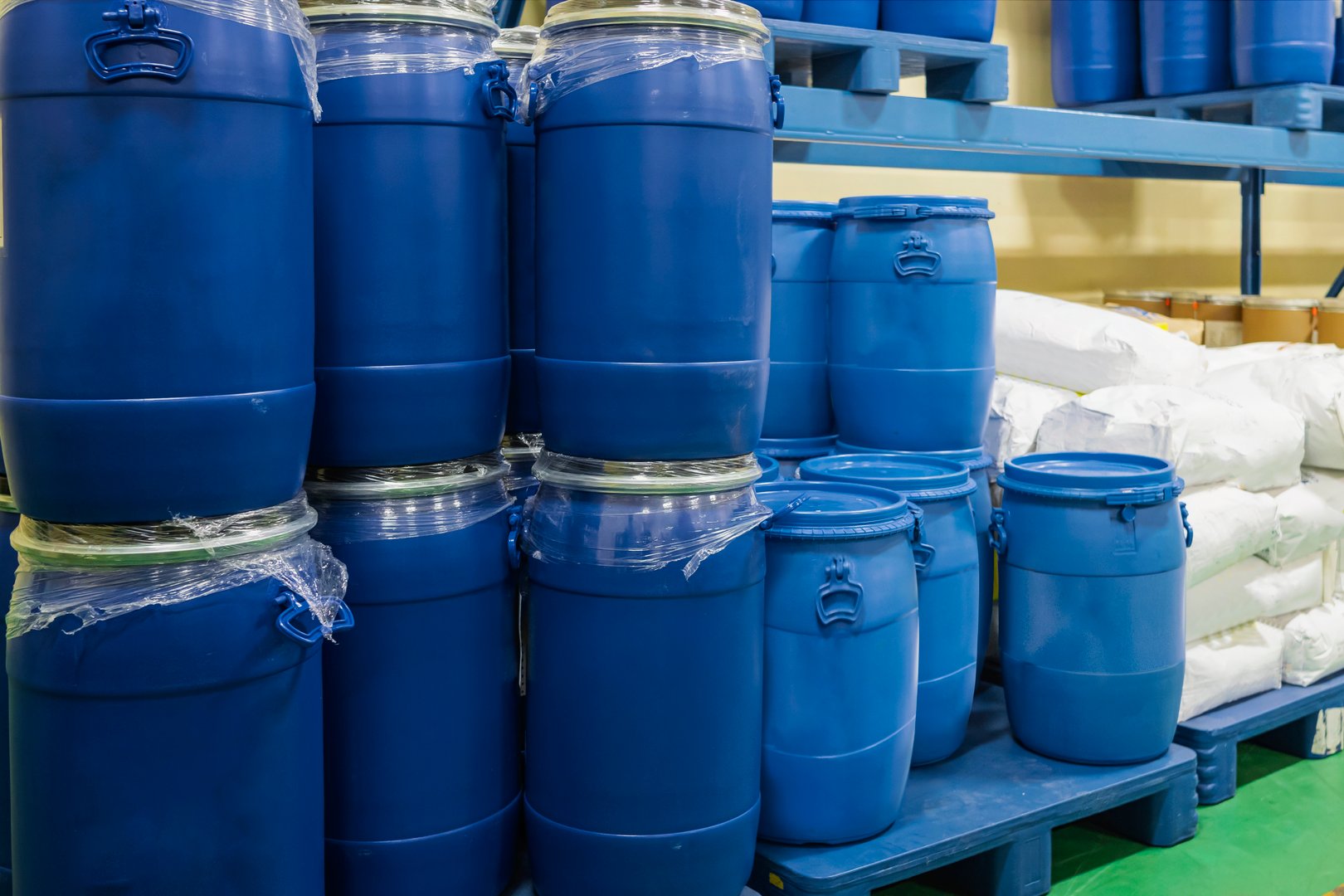 Closeup view of barrels stacked on top of each other. Blue plastic tanks on pallets in a chemical warehouse