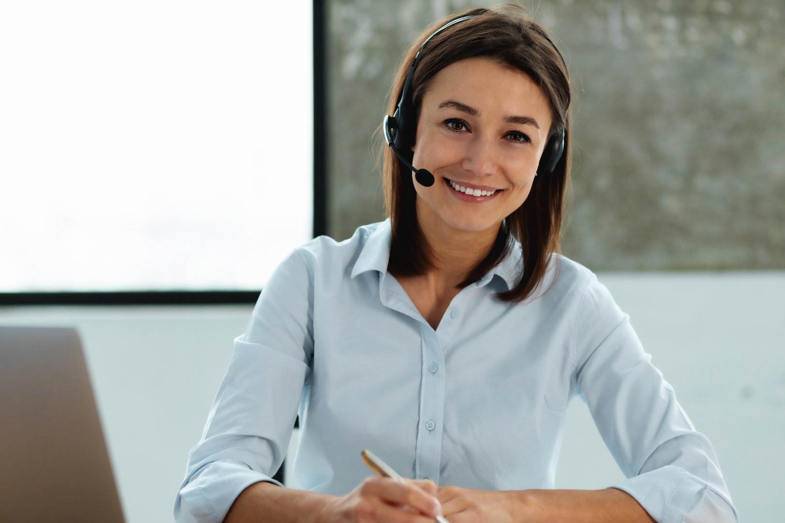 Woman customer support phone operator with headset working. Portrait beautiful caucasian young female call center worker looking at the cameras, smiles friendly