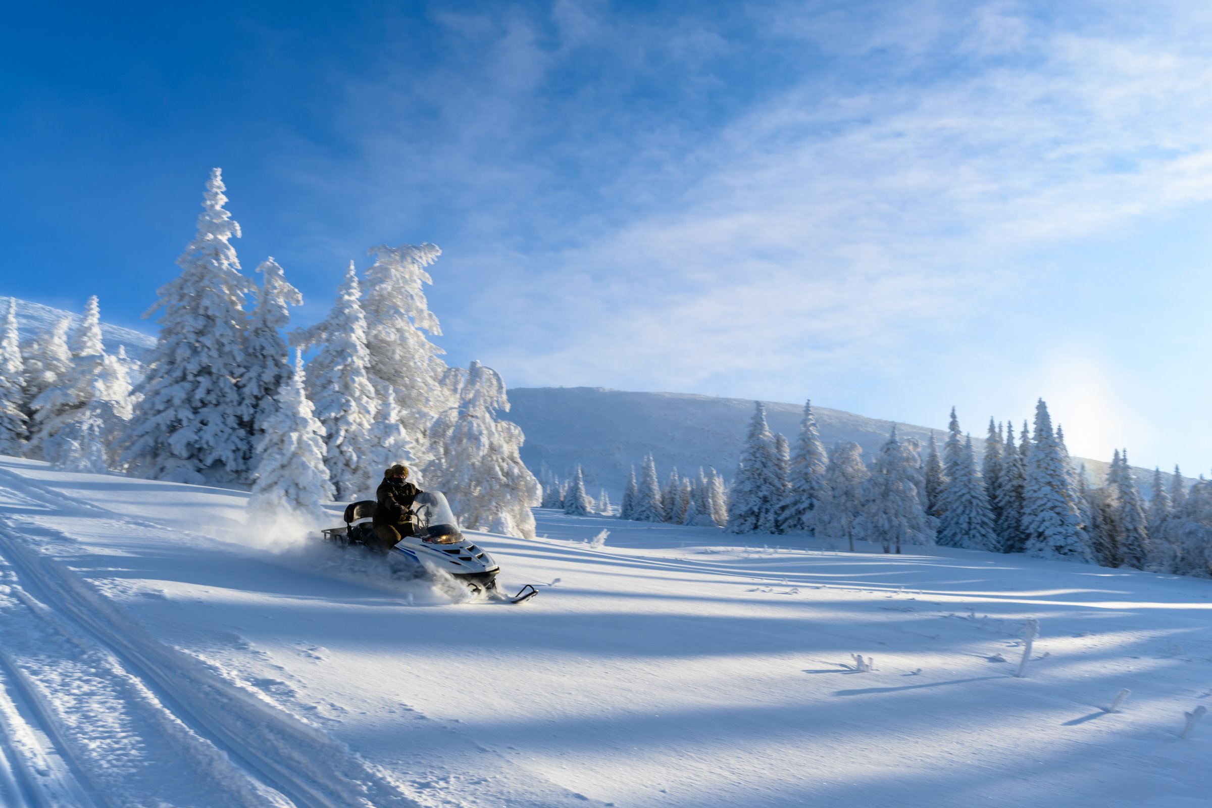 A man is riding snowmobile in mountains. A panoramic view of the covered with snow trees in the snowdrifts. Magical winter forest. Nature winter landscape.