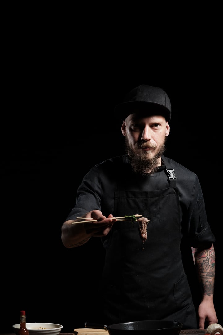 Close up of chef's hands tasting beef noodle bowl with chopsticks