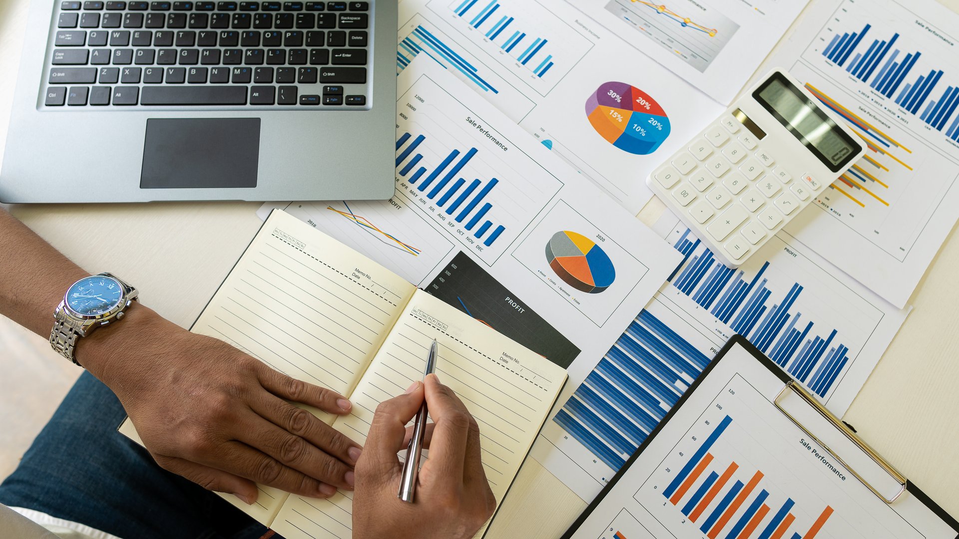 Businessman holding pen pointing to marketing graph and working on the online working concept with financial documents and analytical calculator calculating chart while sitting at office top view
