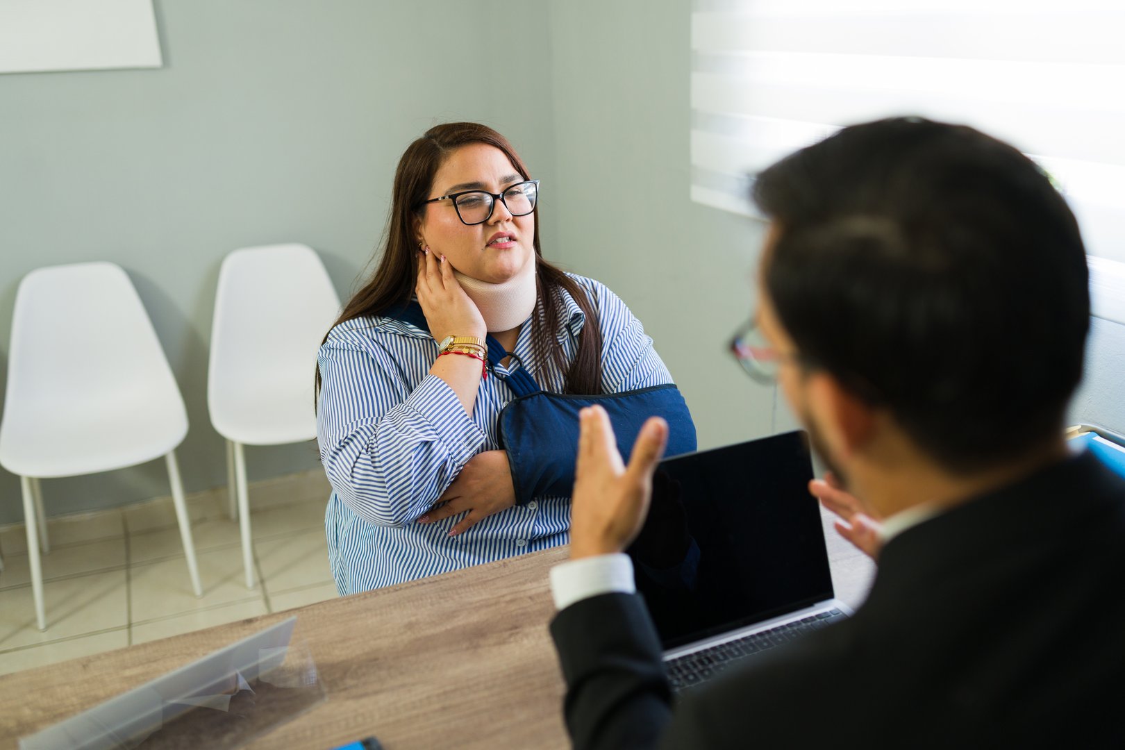 Woman with neck brace and arm sling consulting with an insurance agent about her personal injury claim in a modern office setup