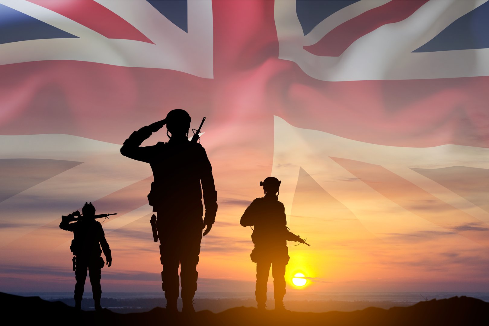 Silhouettes of a soldiers with United Kingdom flag against the sunset. Background for Remembrance Day. United Kingdom Armed Forces concept