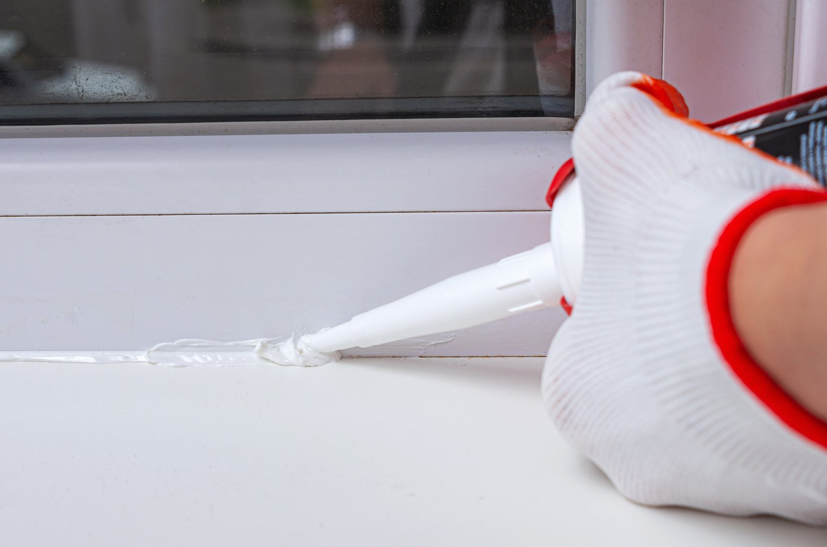 Person's hand applying silicone sealant on window.