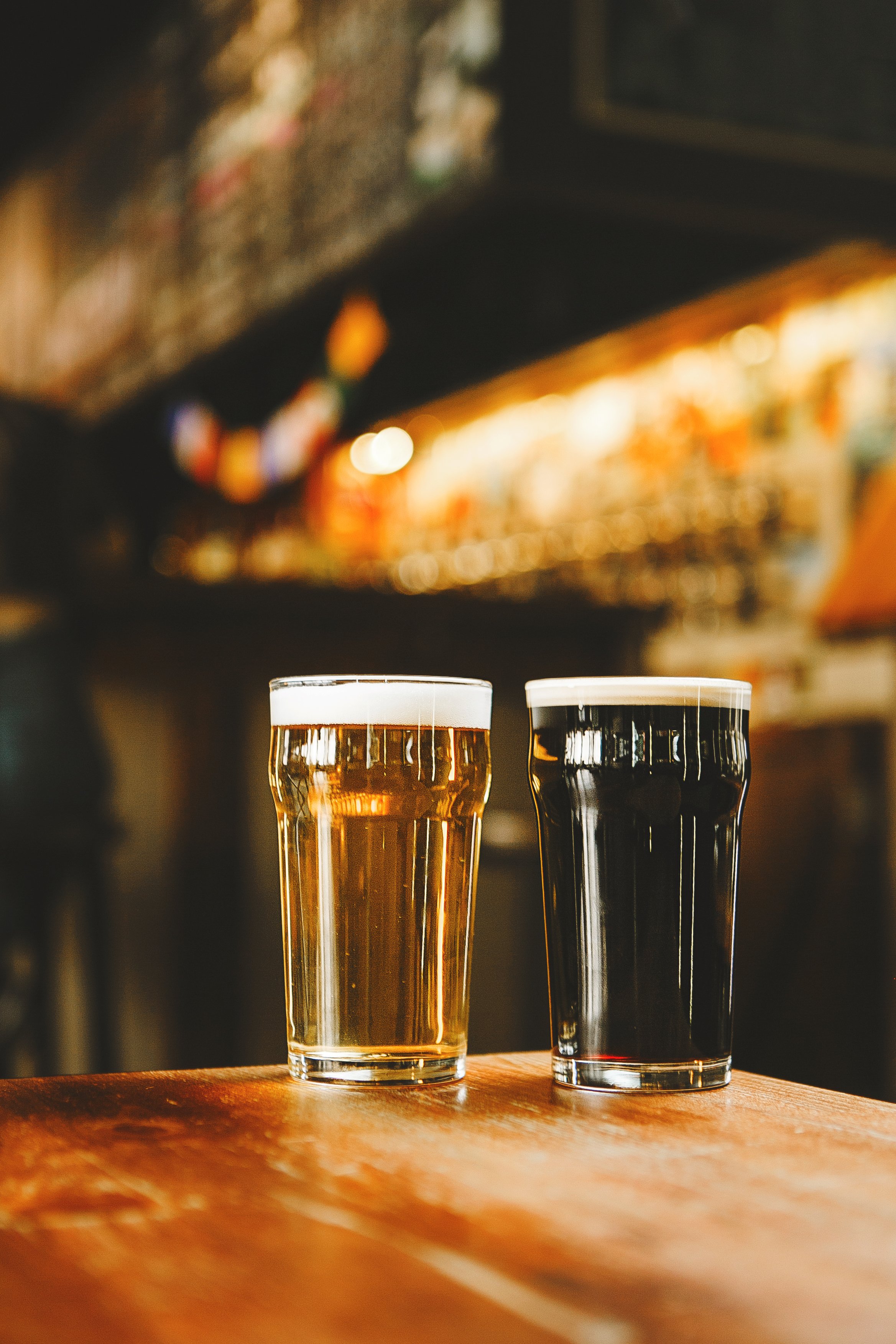 Two glasses of beer sit on wooden table, with one light and one dark brew.