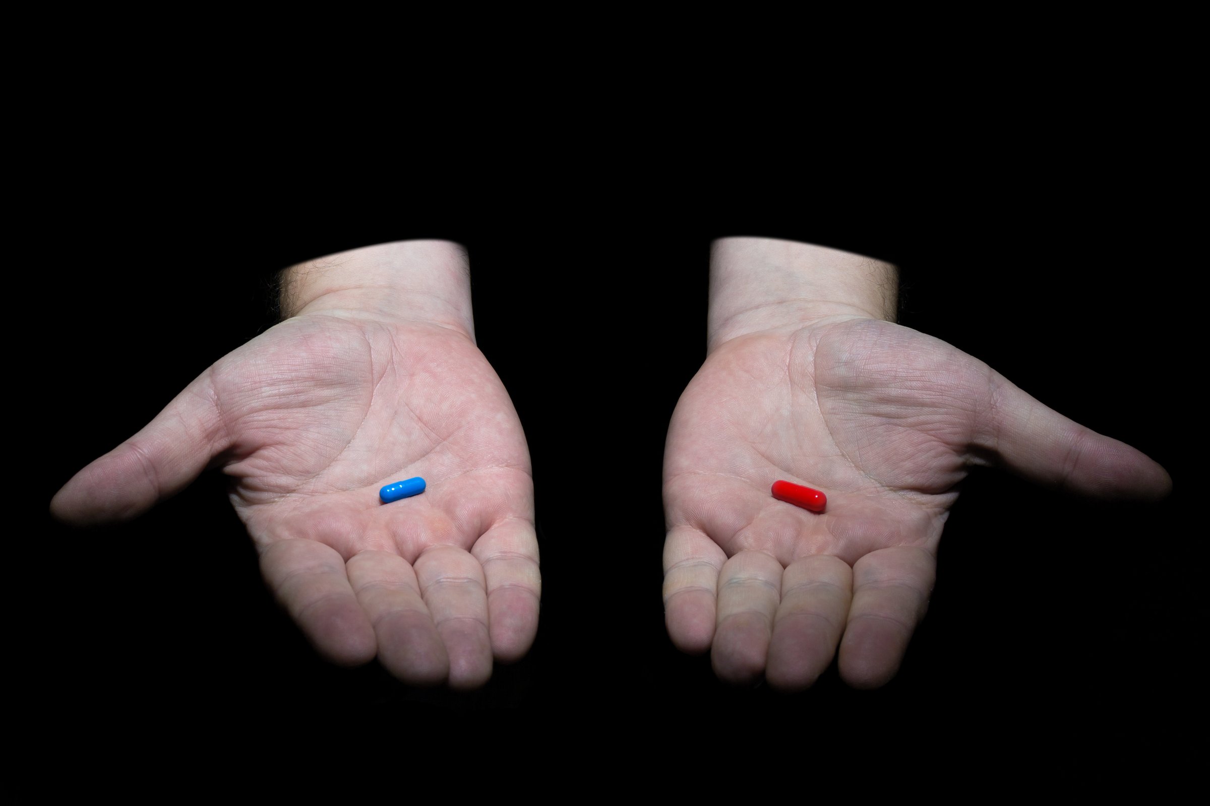 Ð¡hoose your destiny concept. Male hands holding red and blue pills capsules on black background