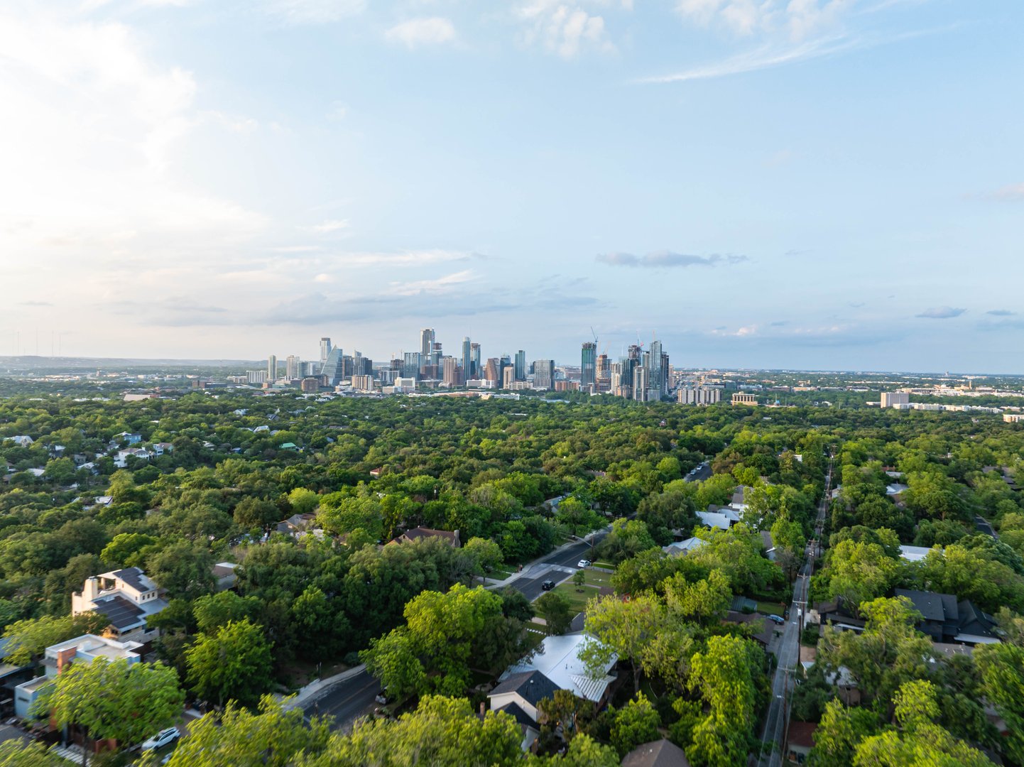 Aerial perspective of Austin, Texas skyline emerging above a verdant tree cover in a residential area, highlighting city's mix of urbanization and natural allure.