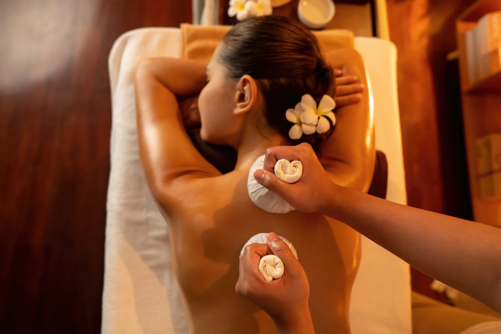 Top view hot herbal ball spa massage body treatment, masseur gently compress herb bag on woman body. Tranquil and serenity of aromatherapy recreation in warm lighting of candle at spa salon. Quiescent