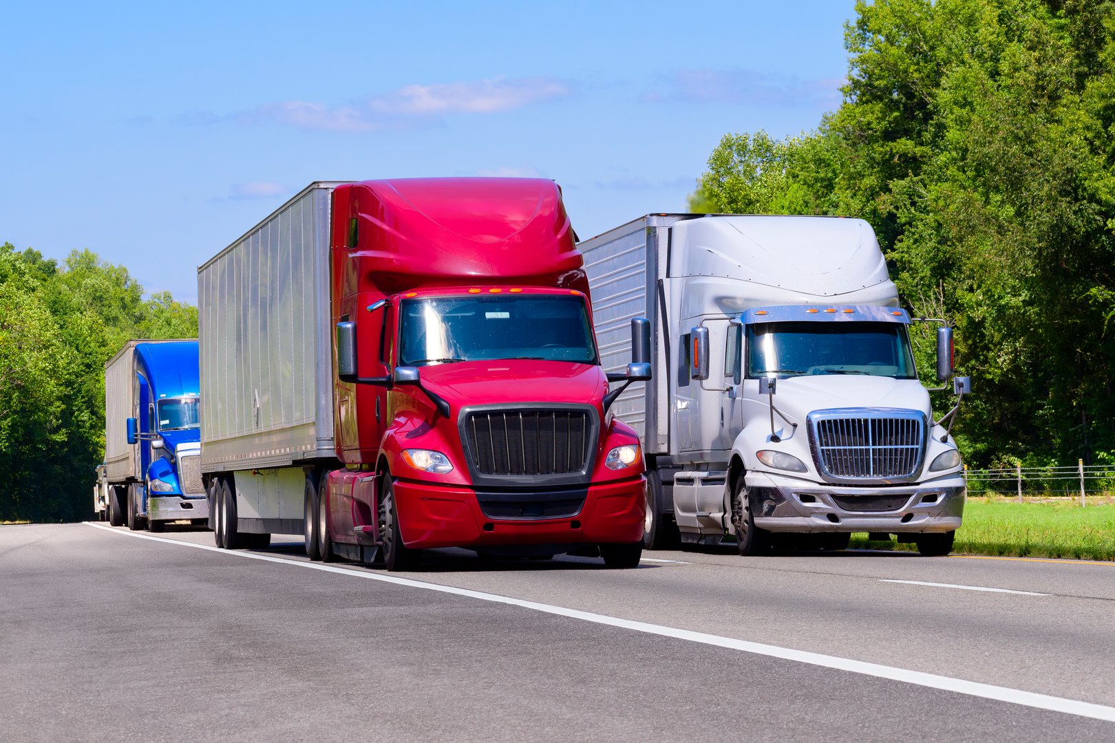 Horizontal shot of red, white, and blue trucks on an interstate with copy space. Heat waves rising from the hot asphalt creates a blurring effect on background trucks and foreground pavement.
