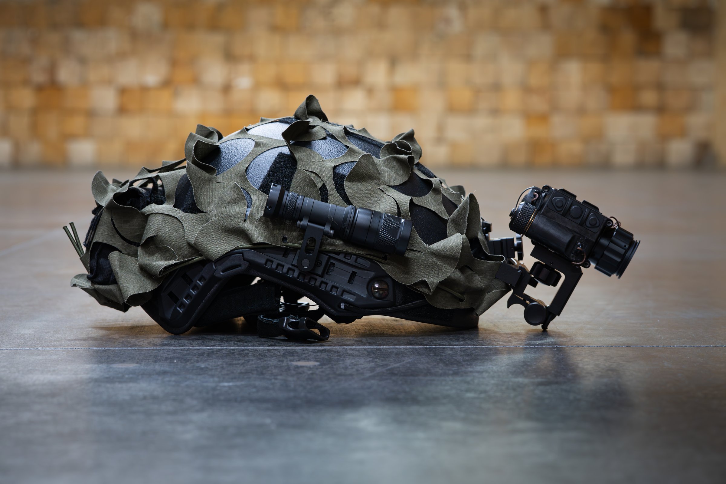 A tactical helmet with a thermal imaging monocular and a flashlight lies on a concrete floor.Close up photo