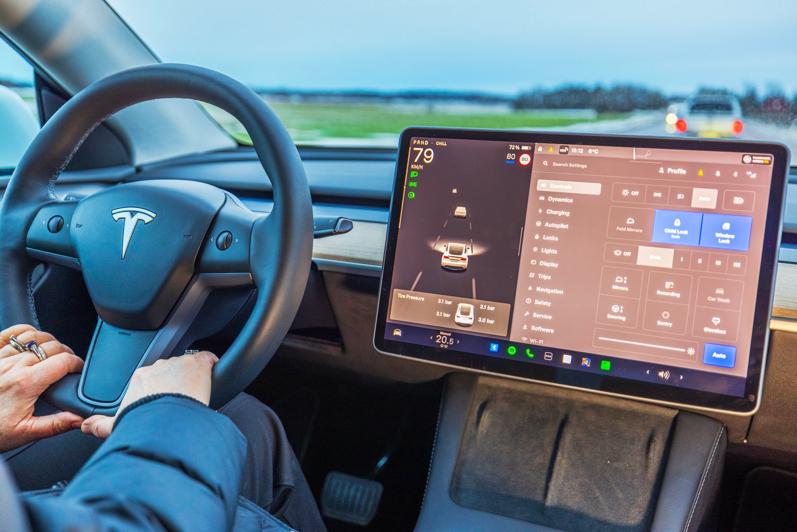 Sweden. Uppsala. 02.16.2025. Close up view of Tesla Model Y driver holding steering wheel while using autopilot and control settings on touchscreen.