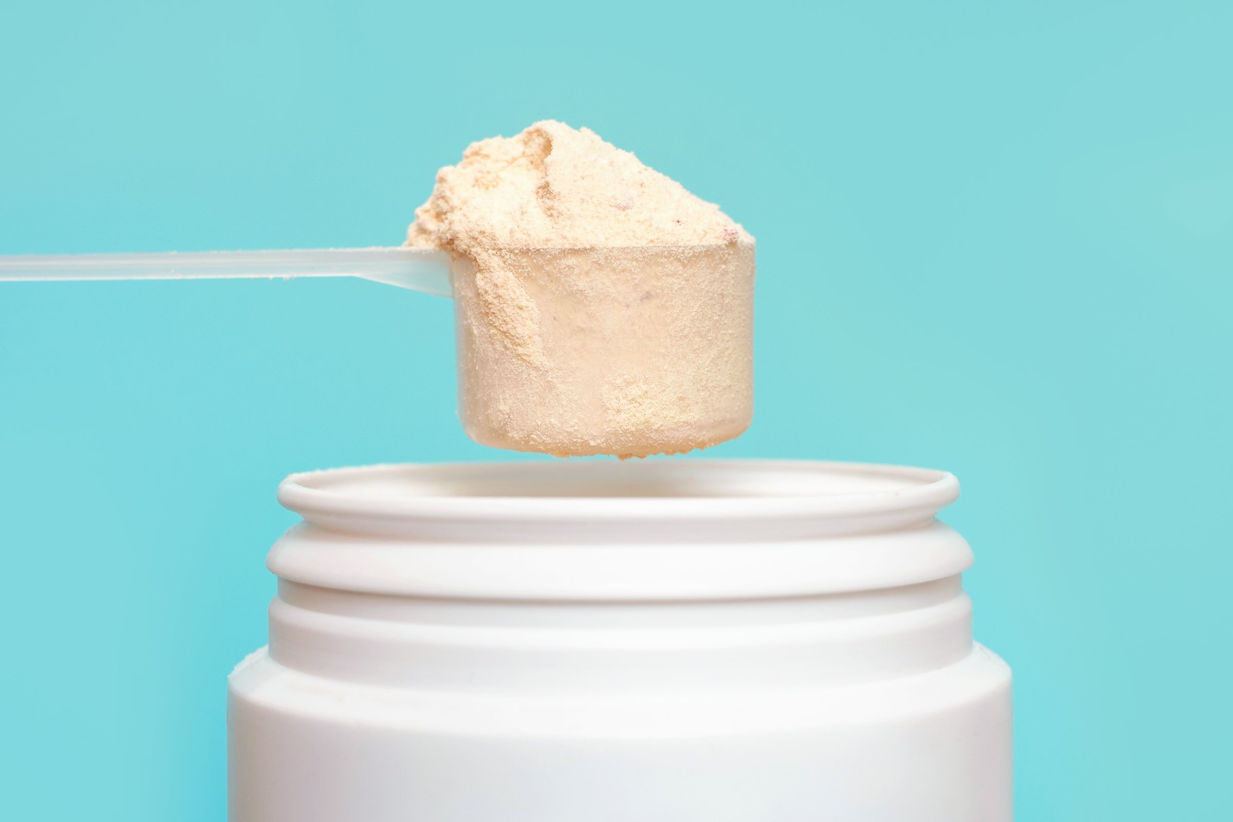 Protein powder in scoop and plastic jar on a blue background.