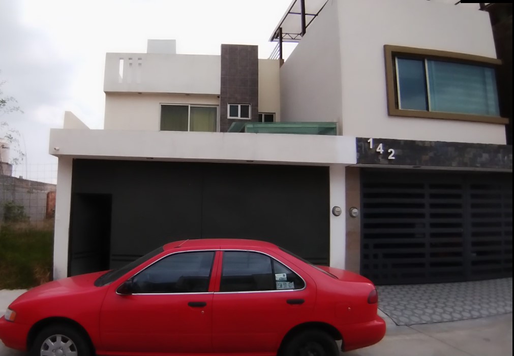 A modern two-story house with a flat roof and large windows, featuring a red sedan parked in front on a paved driveway.