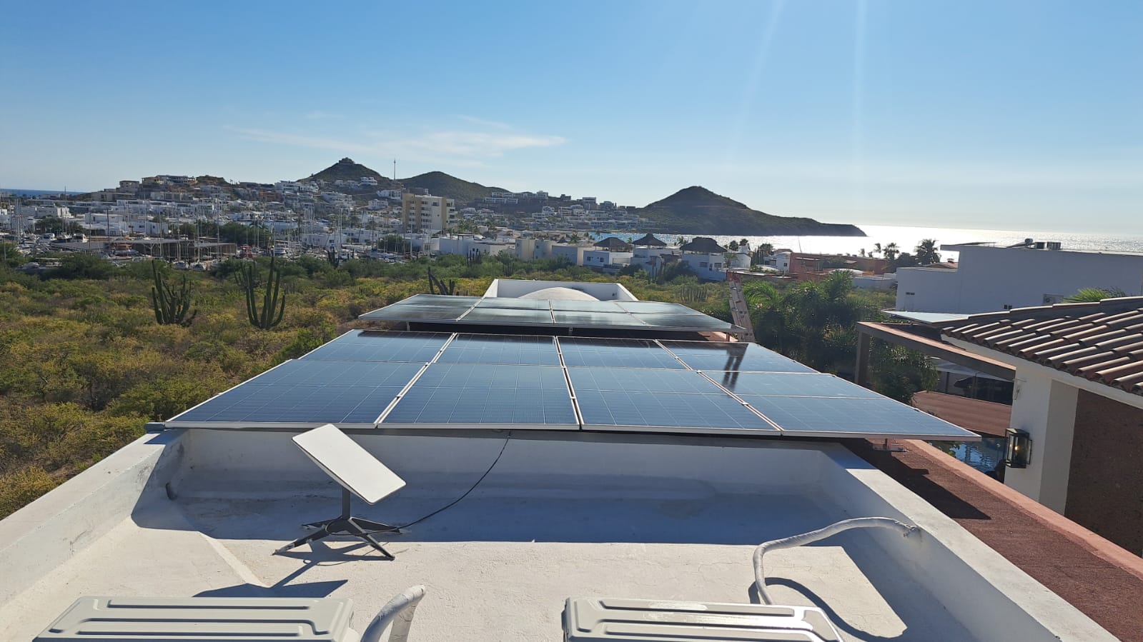 Rooftop with solar panels overlooking a coastal cityscape with hills and distant ocean view under a clear blue sky.