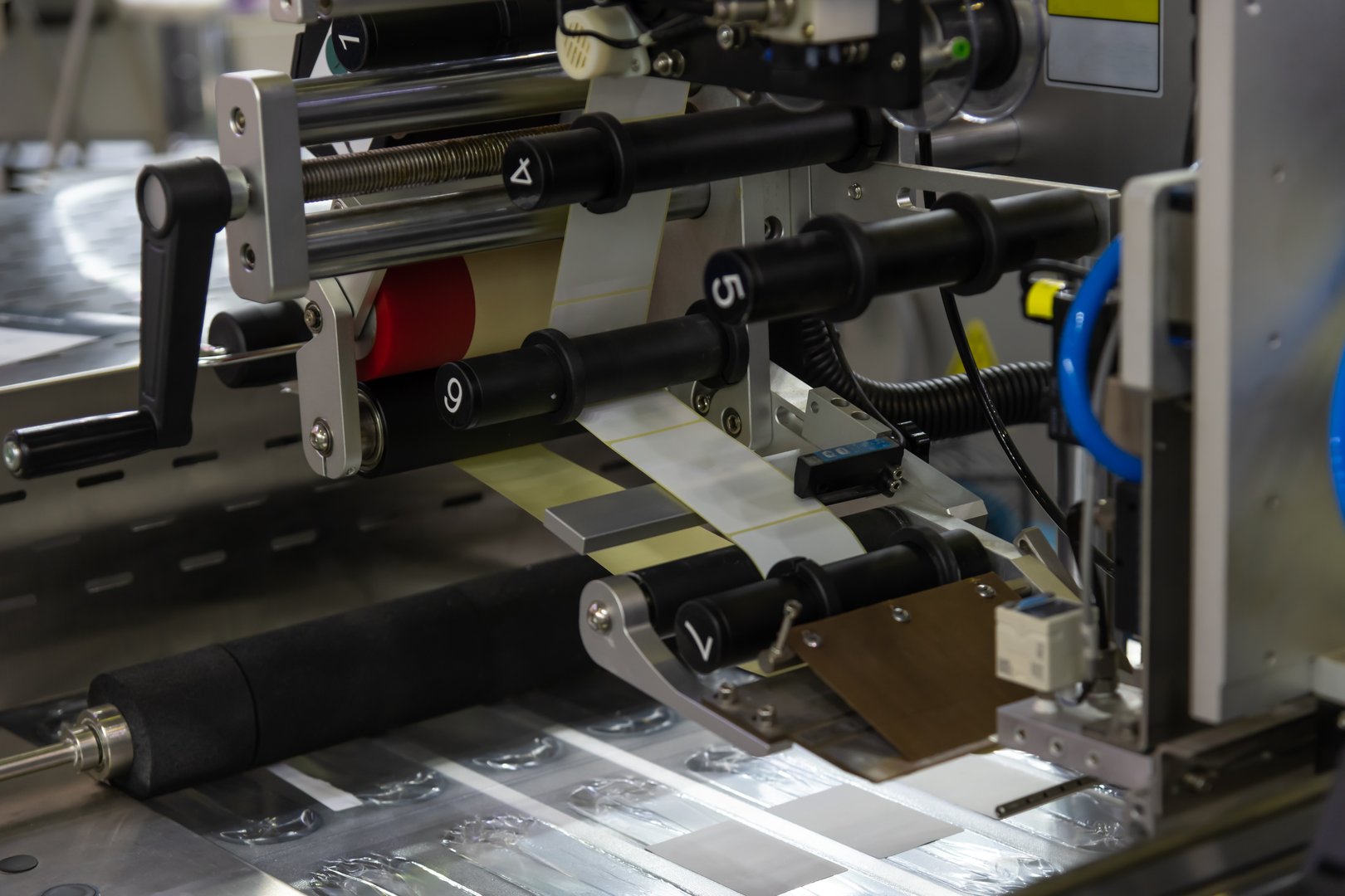 A printing machine is actively running, applying labels onto a roll of material within a manufacturing facility. The setting reflects a modern industrial environment during the afternoon.