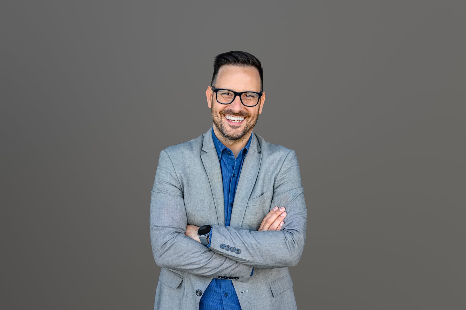 Portrait of inspired male CEO in eyeglasses and with arms crossed posing isolated on gray background