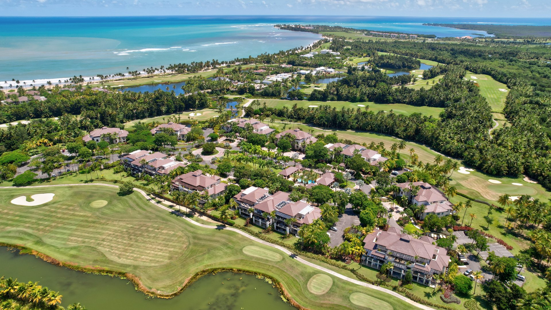 This aerial view showcases the stunning Bahia Beach Resort in Rio Grande, Puerto Rico.  Lush green fairways weave through the resort's elegant villas, leading to the pristine beach and sparkling turquoise waters of the Atlantic Ocean.