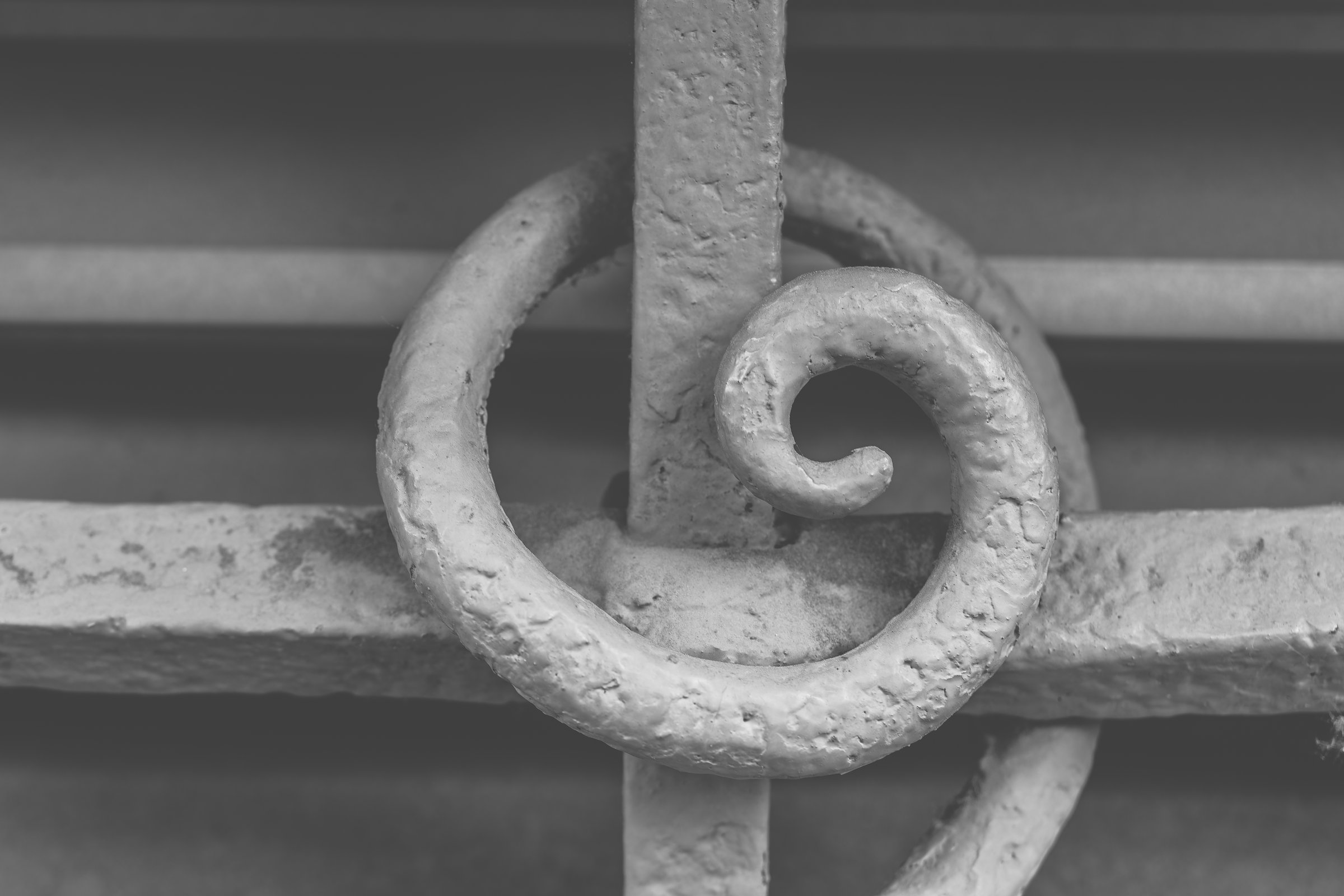 Curved and spiraled iron elements form a captivating design on an aged gate, reflecting artistry and history in a charming city neighborhood.
