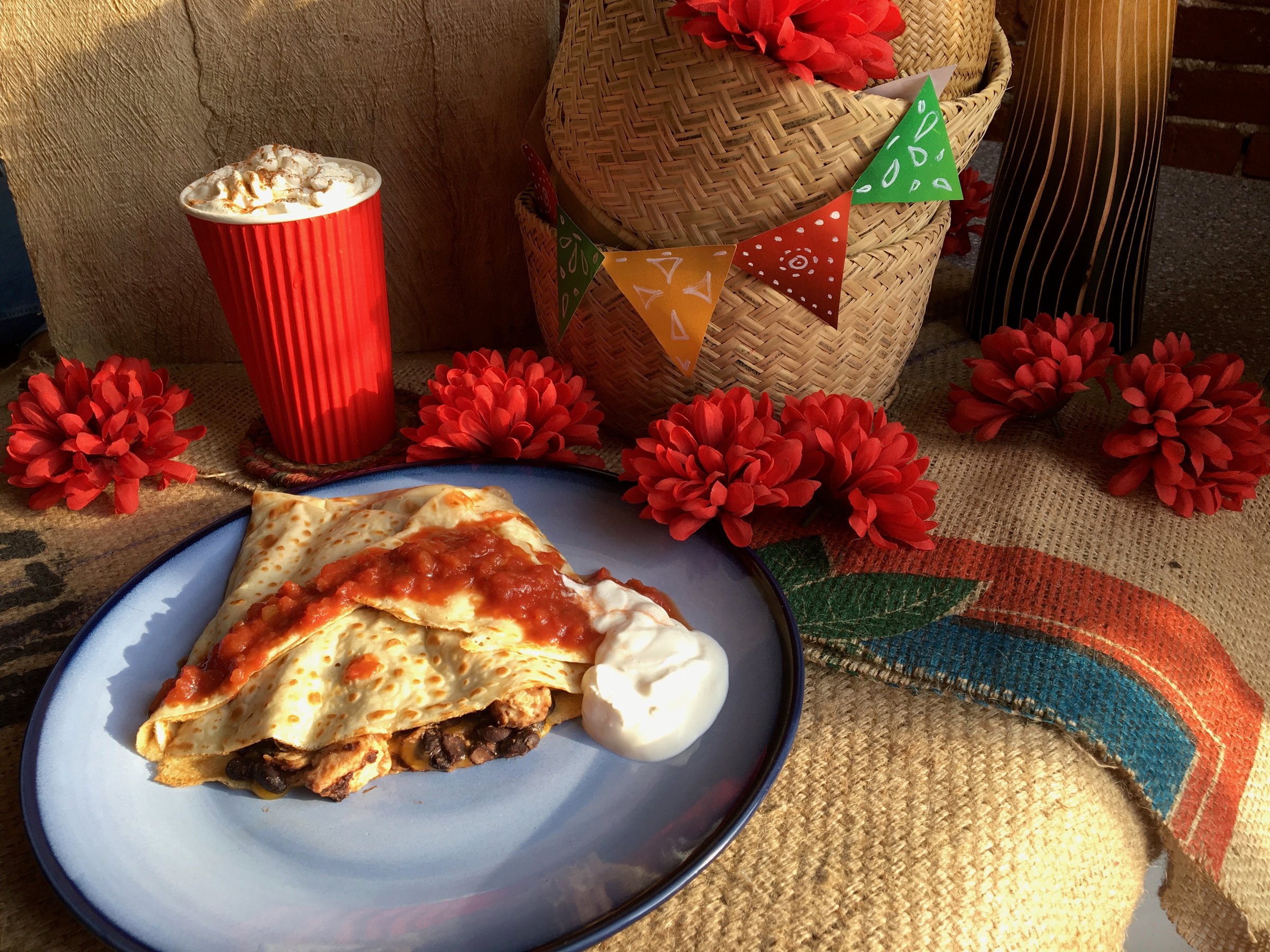 Mexican crepe on a plate and a hot drink displayed with hispanic decorations.