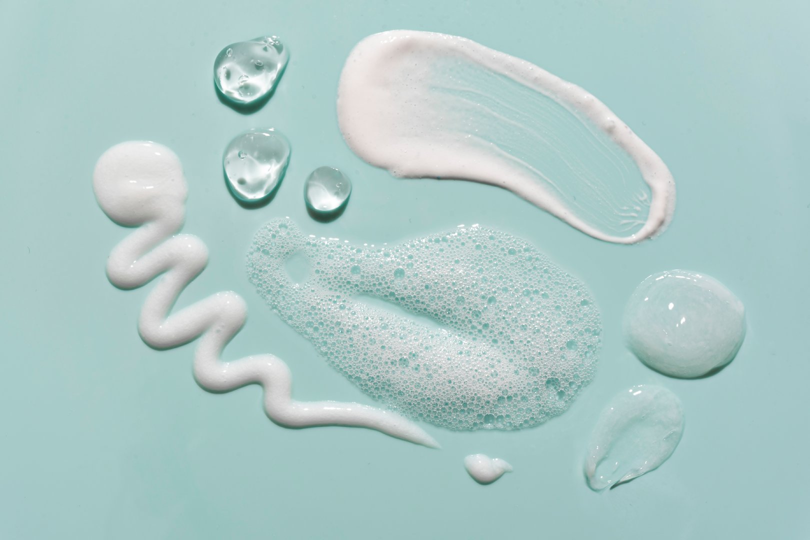 Various cosmetic skin care products smear swatches on green blue background close up. Makeup removal products samples - washing gel, foam mousse and milk.