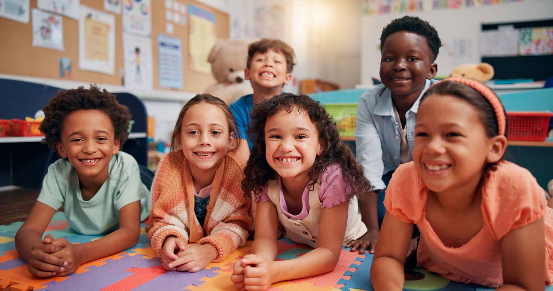 Children, group and smile on floor in classroom, portrait and excited with diversity, education and scholarship. School kids, happy and lying on mat with friends, solidarity and learning at academy