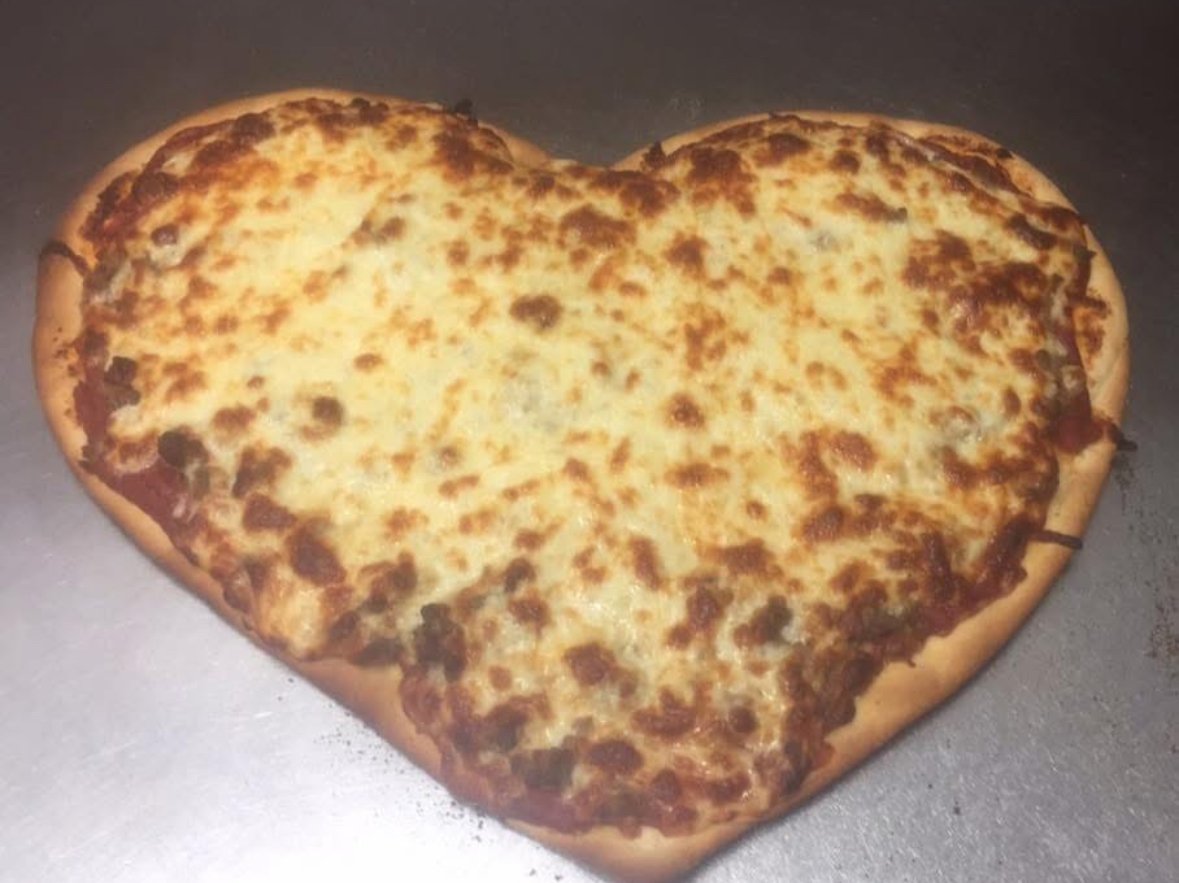 Heart-shaped cheese pizza with melted golden-brown cheese on a metal surface.