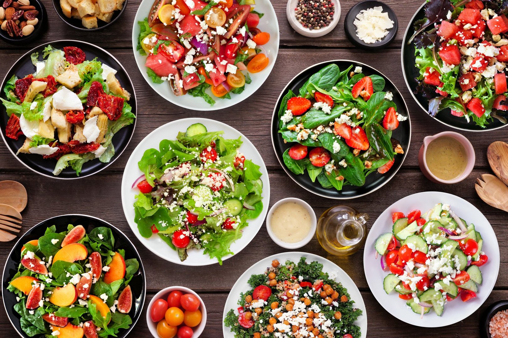 Variety of delicious fresh salads. Above view table scene on a dark wood background. Summer food concept.