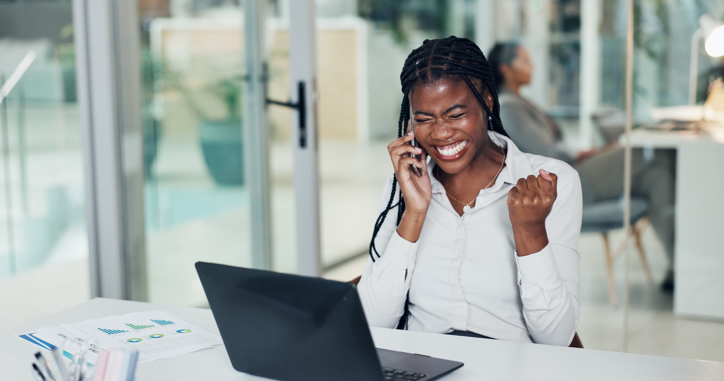 African woman celebrating business success while using laptop and phone