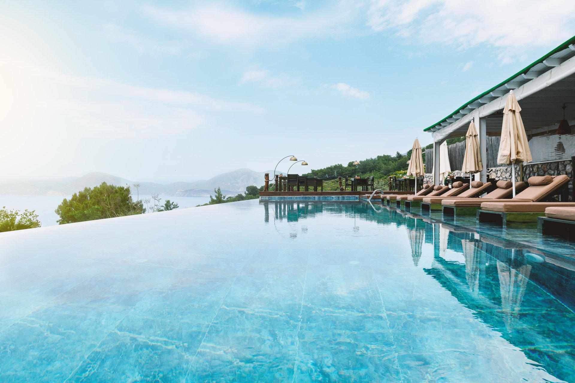 A daytime photo of a hotel's shared infinity pool with sun loungers during summer season, showcasing luxurious relaxation.