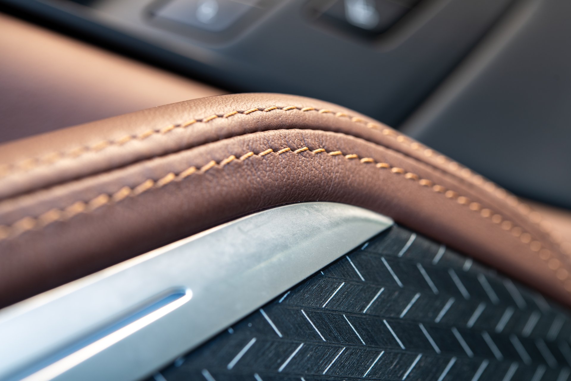 A detailed view of luxurious brown leather upholstery featuring intricate stitching, complemented by sleek metallic accents, enhancing automotive interior aesthetics and comfort.